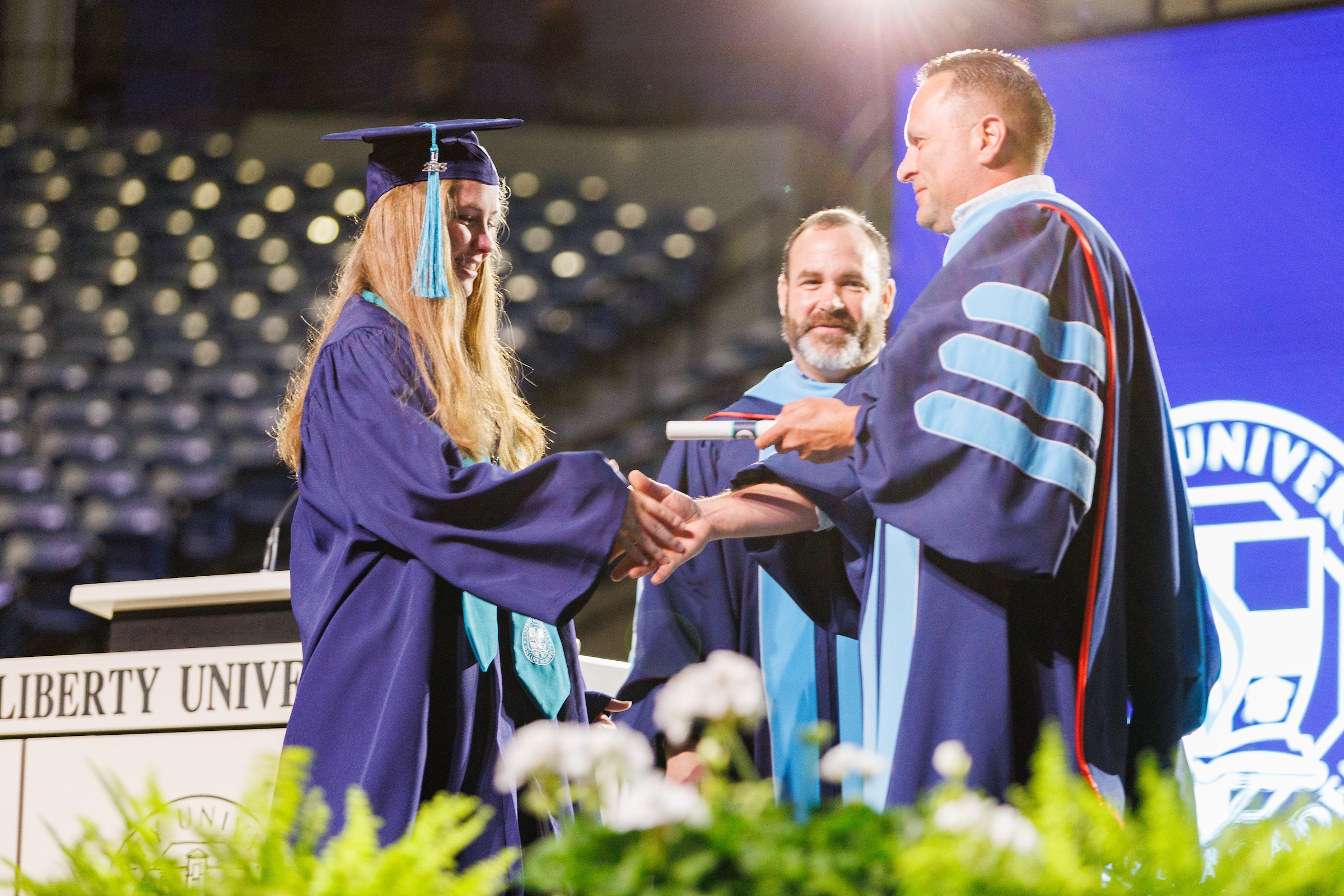 Female LUOA graduate on stage receiving her diploma from her father